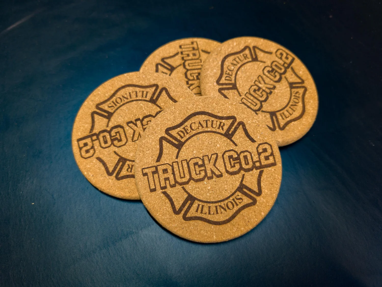 Custom laser-engraved round cork coaster with firefighter helmet shield design